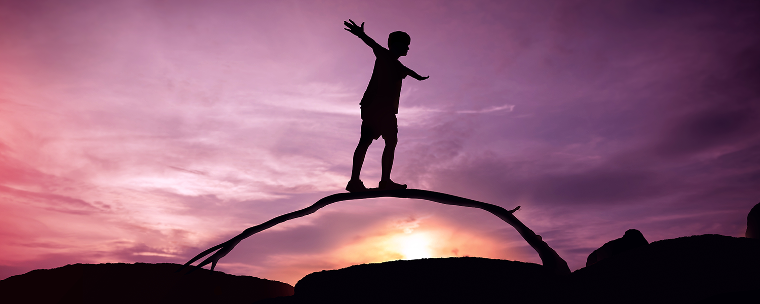 The silhouette of a person balancing on an arched branch.