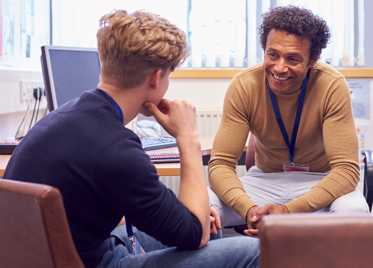 A black man speaks with a young white man during a therapy session.