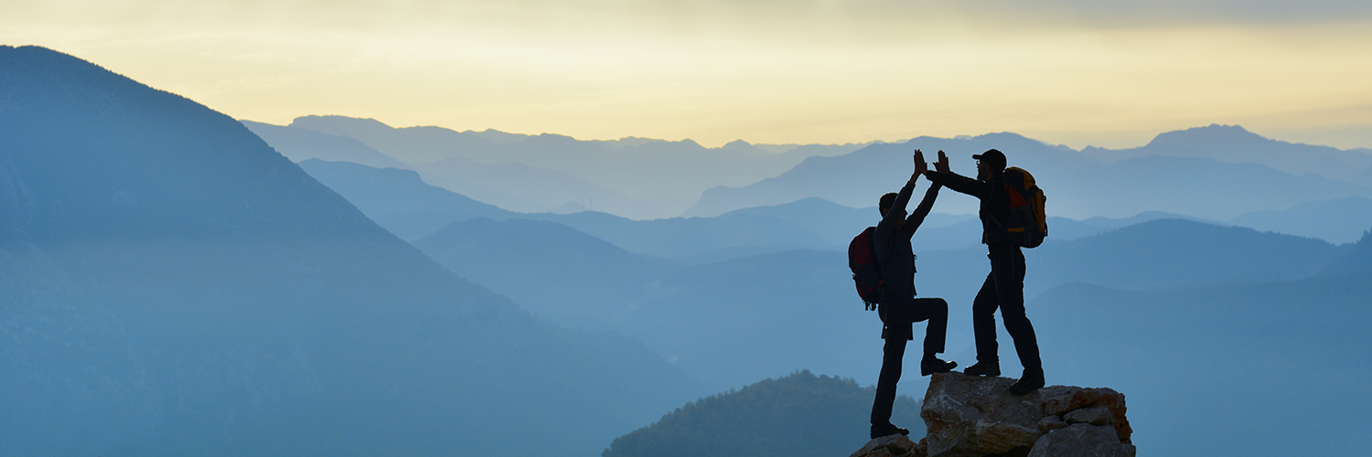 Silhouette of two people on top of a mountain high-fiving.